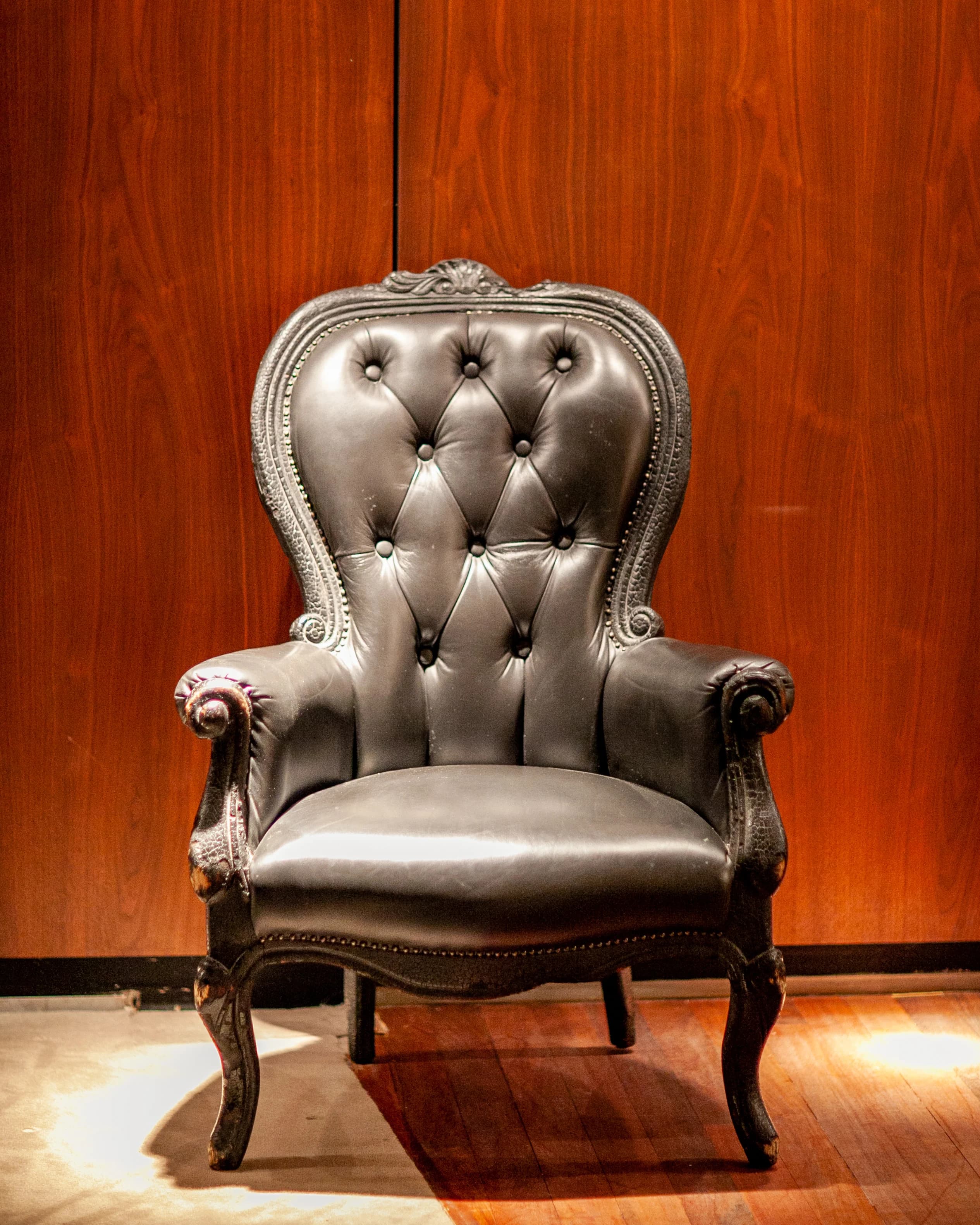 A vintage tufted leather armchair against a warm wood-paneled wall.